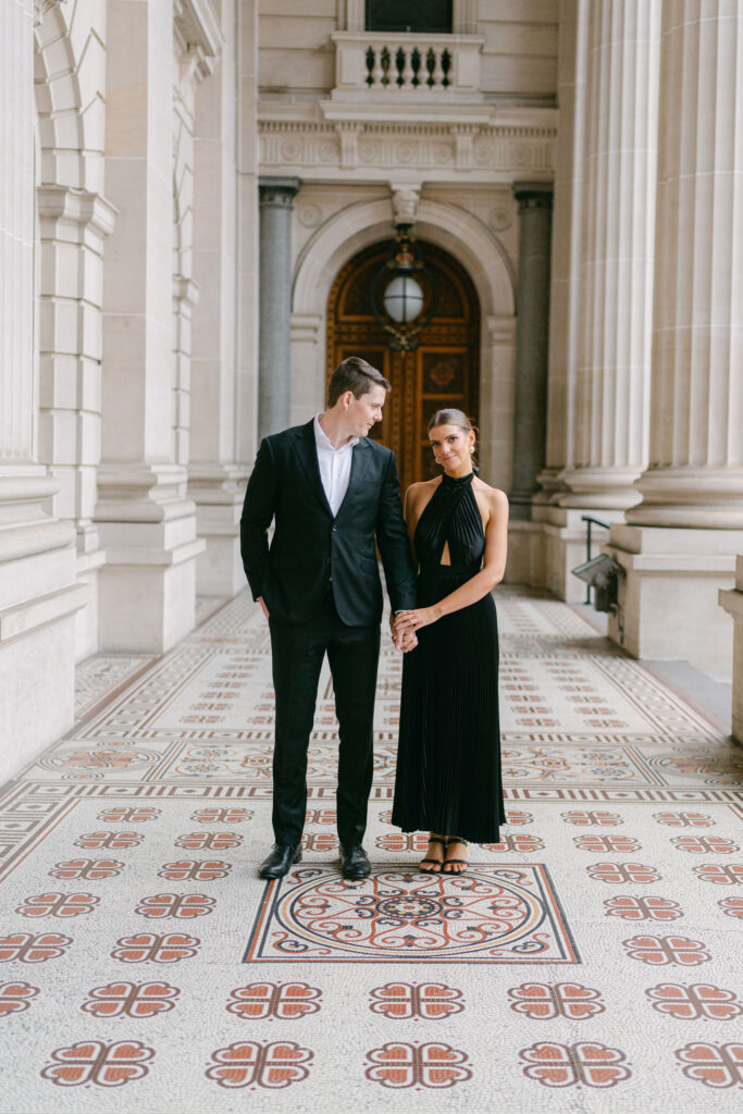 Smart couple dressed in black standing under the portico of the Melbourne's Parliament House